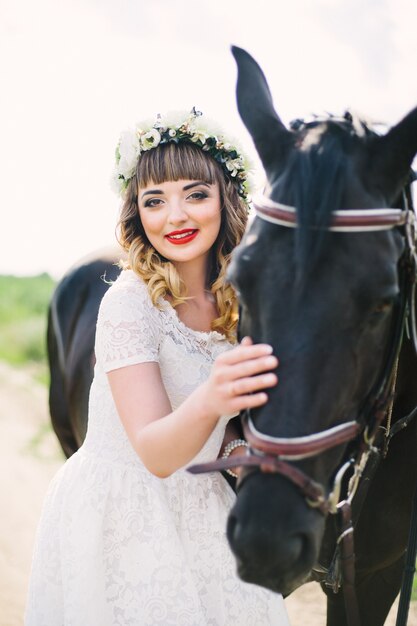 Mädchen mit roten Lippen in einem weißen Kleid neben einem schwarzen Pferd