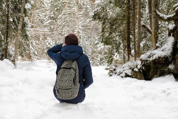 Mädchen mit Rucksack sitzt in einem schneebedeckten Nadelwald Bewölkter Wintertag