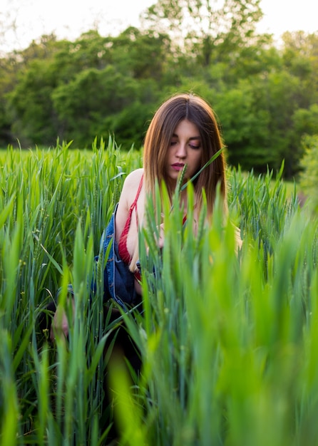 Mädchen mit schönen Haaren, die auf einem grünen Feld in den Strahlen der untergehenden Sonne sitzen.