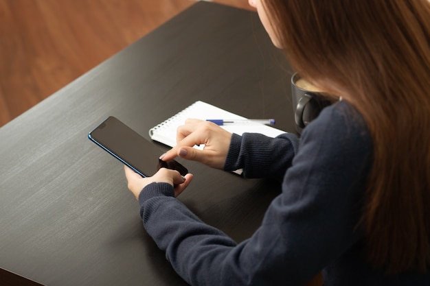 Mädchen mit Smartphone an einem Tisch in einem Café mit Kaffee und einem Notebook in Bürokleidung