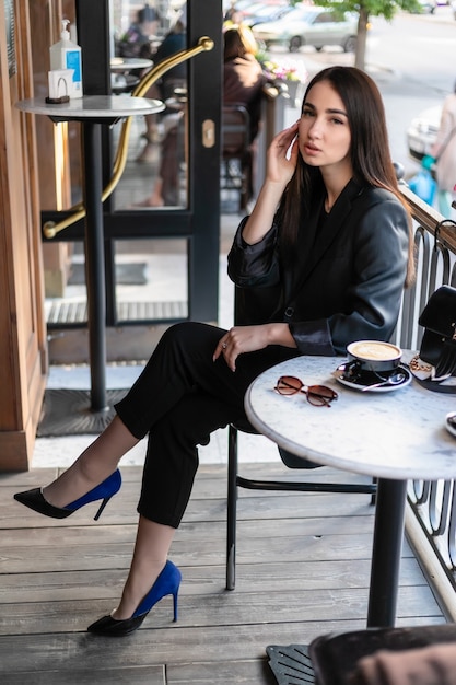 Mädchen mit Sonnenbrille sitzt in einem Café, Café, sitzt auf einem Stuhl in der Stadt mit roten Blumen und trägt eine Sonnenbrille