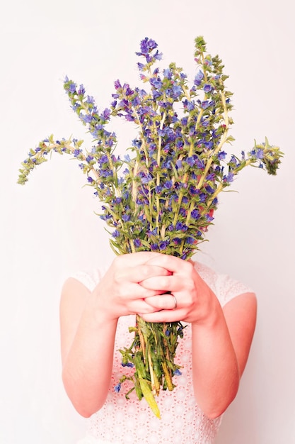 Mädchen mit Strauß violetter Feldblumen auf dem weißen Hintergrund.