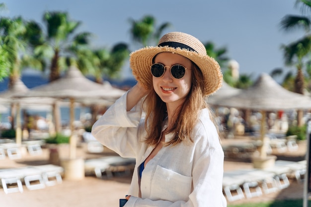 Mädchen mit Strohhut am Hotelpool mit Sonnenschirmen und Palmen herum