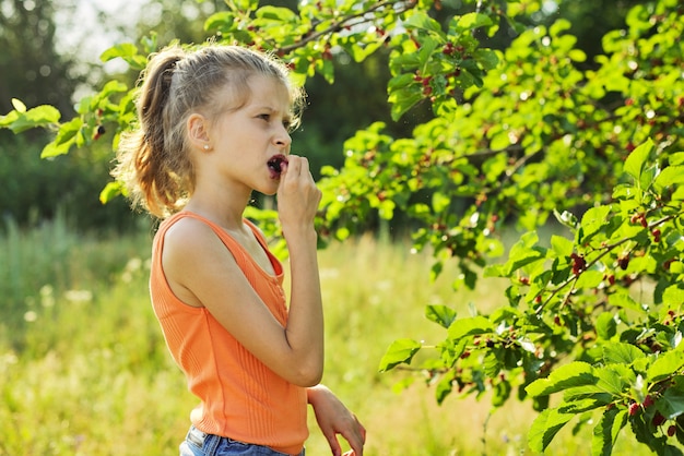 Mädchen mit Vergnügen, das köstliche süße reife Beeren vom Maulbeerbaum isst