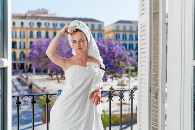 Mädchen mit verletztem Gesicht steht auf dem Balkon und wickelt den Körper mit einem Laken und einem Handtuch auf den Kopf