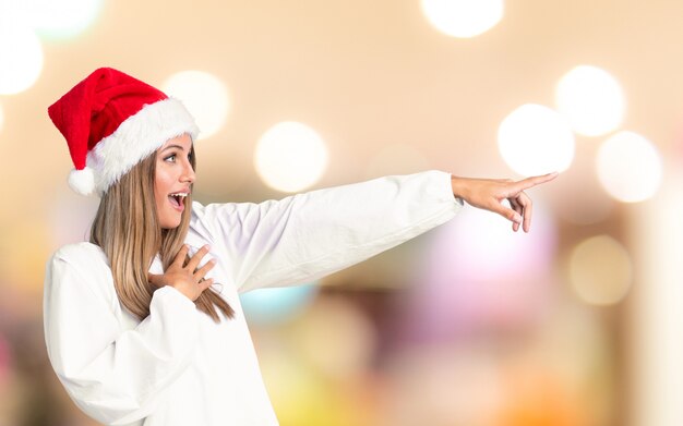 Mädchen mit Weihnachtshut Finger auf die Seite über unfocused Hintergrund zeigend