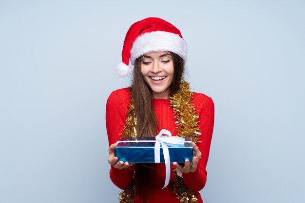 Mädchen mit Weihnachtshut und Anhalten eines Geschenks über getrenntem Blau