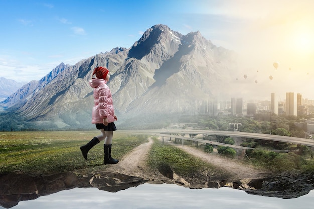 Mädchen mit Wollmütze und Gummistiefeln geht alleine mit Landschaft im Hintergrund. Gemischte Medien