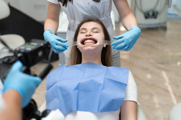 Mädchen mit Zahnkappen, die in der Arztpraxis für Zahnaufhellung sitzen. Verfahren in der Zahnheilkunde. Zahnaufhellung mit ultraviolettem Licht