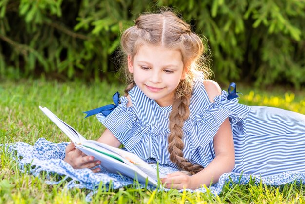 Mädchen mit Zöpfen, die ein Buch auf dem Rasen lesen.