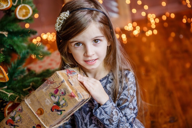 Mädchen nahe dem Weihnachtsbaum mit einem Geschenk in ihren Händen