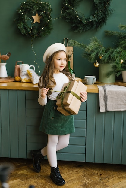 Mädchen öffnet ein Weihnachtsgeschenk in der Küche, dekoriert für das neue Jahr