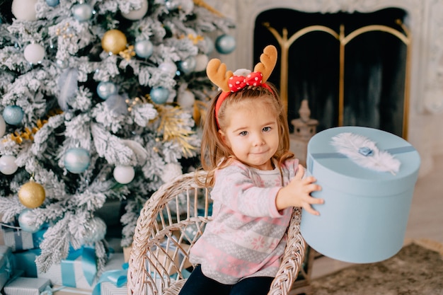 Mädchen packt Geschenk auf Hintergrund des Weihnachtsbaumes aus