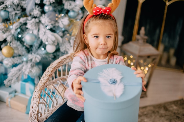 Mädchen packt Geschenk auf Hintergrund des Weihnachtsbaumes aus