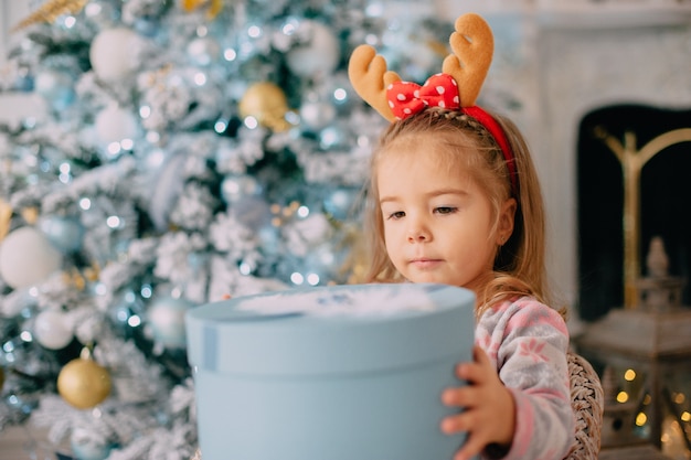 Mädchen packt Geschenk auf Hintergrund des Weihnachtsbaumes aus