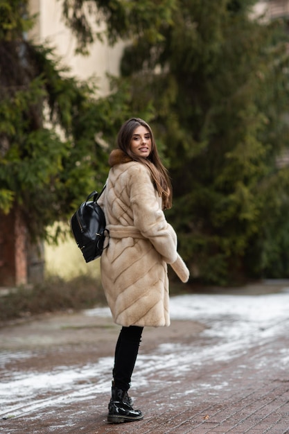 Mädchen posiert auf der Straße im Winter Hintergrund Glamouröse lustige junge Frau mit einem Lächeln, das stilvollen grauen langen Pelzmantel trägt Pelz- und Modekonzept Schöne Menschen