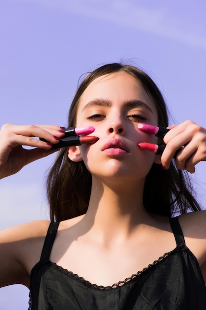 Mädchen posiert mit rosa Lippen und Lippenstiften am blauen Himmel