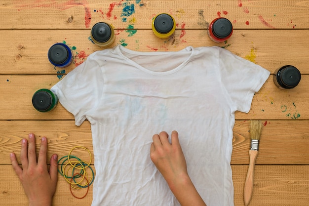 Mädchen rollt ein weißes T-Shirt für die Anwendung der Krawattenart auf. Fleckiger Stoff im Tie-Dye-Stil.