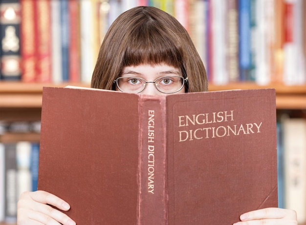 Mädchen schaut über englisches Wörterbuch und Bücher