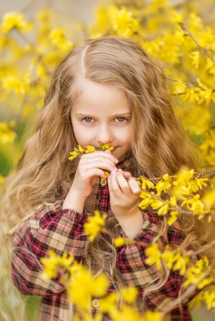 Mädchen schnüffelt gelbe Blumen. Ein Kind vor dem Hintergrund der Forsythie. Frühlingsporträt eines Kindes mit Blumen in ihren Haaren