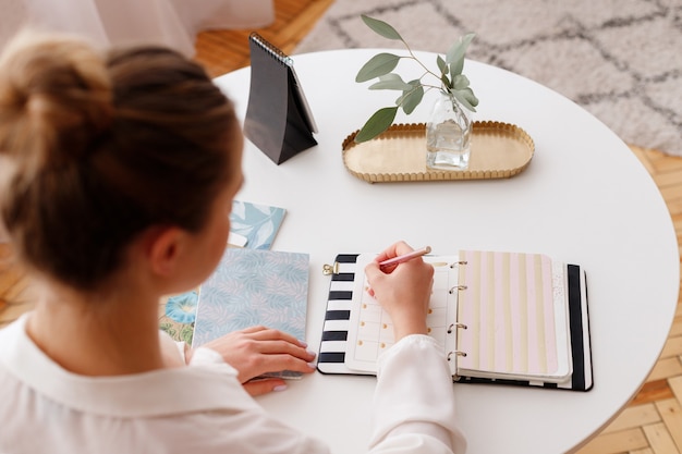 Mädchen schreibt in ein Notizbuch im Büro. Draufsicht auf den Arbeitsplatz