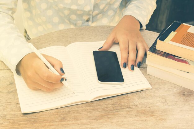 Mädchen schreibt in ein Notizbuch mit Handy und Büchern