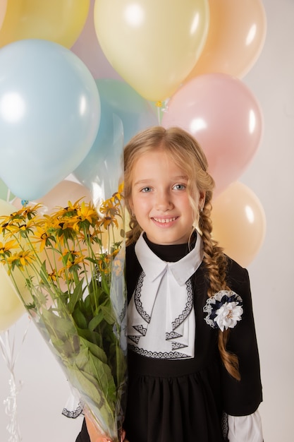 Mädchen Schulmädchen, Schülerin der ersten Klasse in Schuluniform auf weißem Hintergrund mit Bällen und Blumen