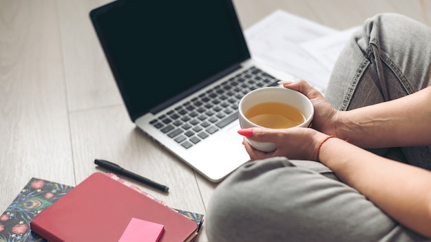 Mädchen sitzen zu Hause auf dem Boden mit einer Tasse Kaffee, Notebooks und ihrem Laptop aus nächster Nähe