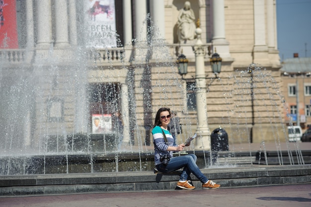 Mädchen sitzt am Brunnen mit Karte und Kamera