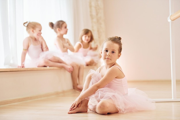 Mädchen sitzt auf der Fensterbank und auf dem Boden Kleine Ballerinas bereiten sich auf die Aufführung vor