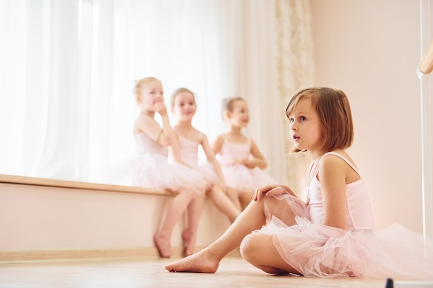 Mädchen sitzt auf der Fensterbank und auf dem Boden Kleine Ballerinas bereiten sich auf die Aufführung vor