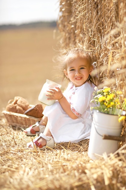 Mädchen sitzt auf einem Feld neben einem Heuhaufen mit einer Dose frischer gedämpfter Kuhmilch