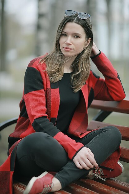 Mädchen sitzt auf einer Gartenbank / schönes Model posiert im Mantel auf Bank im Stadtpark sitzend, schönes Mädchen