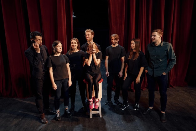 Mädchen sitzt auf Stuhl und weint Gruppe von Schauspielern in dunkler Kleidung bei der Probe im Theater