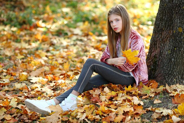 Mädchen sitzt in der Nähe eines großen Baums im Herbstpark