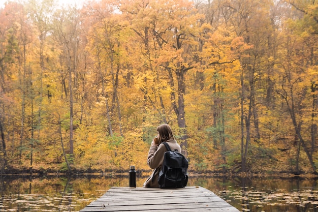 Mädchen sitzt nahe See im Herbst und trinkt Kaffee