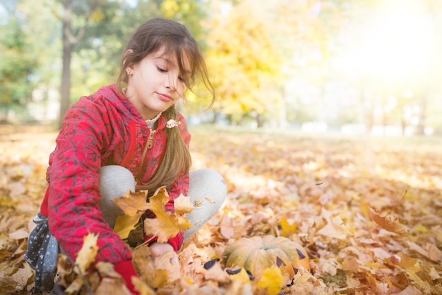 Mädchen spielen mit gelben Ahornblättern beim Gehen im sonnigen Herbstpark