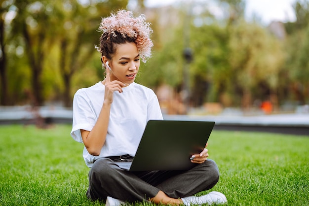 Mädchen sprechen per Videoanruf mit Kollegen am Laptop, die im Park sitzen. Junge Freiberuflerin