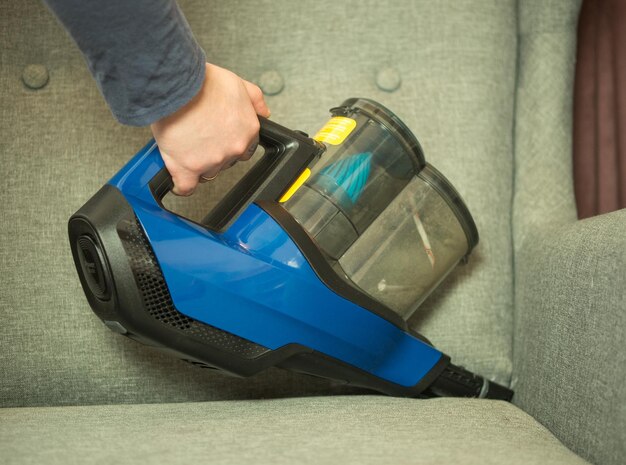 Foto mädchen staubsaugt das sofa, reinigt die wohnung mit einem drahtlosen staubsauger