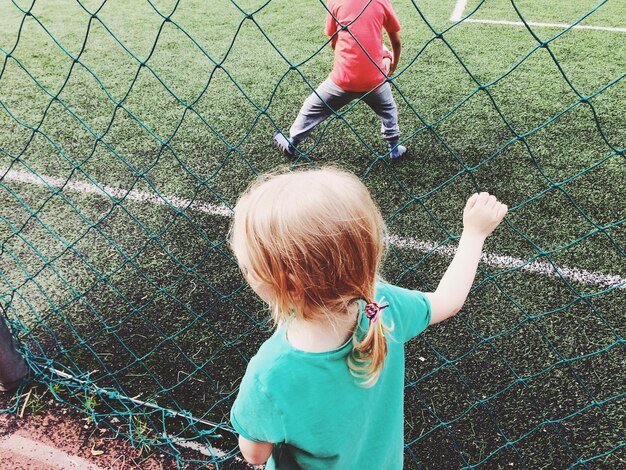 Foto mädchen steht am spielplatz vor dem netz