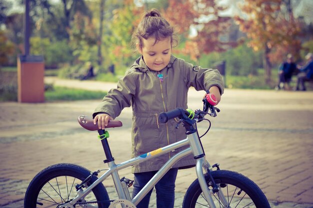 Foto mädchen steht mit dem fahrrad auf dem fußweg im park