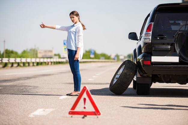 Mädchen steht mit erhobener Hand und fängt ein vorbeifahrendes Auto.