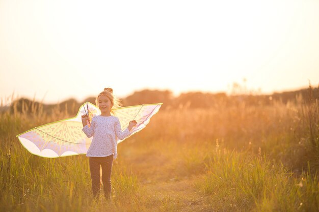 Mädchen steht mit Flügeln im Feld und lernt, einen Drachen zu fliegen. Outdoor-Entertainment im Sommer, Natur und frische Luft. Kindheit, Freiheit und Sorglosigkeit. Kinderträume und Hoffnung