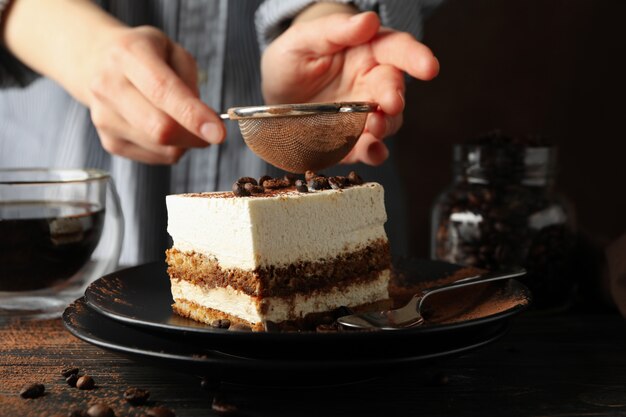 Mädchen streut Pulver auf Tiramisu. Zusammensetzung mit leckerem Kuchen auf hölzernem Hintergrund