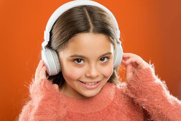 Mädchen süßes kleines Kind tragen Kopfhörer Musik hören. Kind hört Musik orange Hintergrund. Empfohlene Musik basierend auf anfänglichem Interesse. Sagen Sie mir, was Sie hören, und ich sage Ihnen, wer Sie sind.