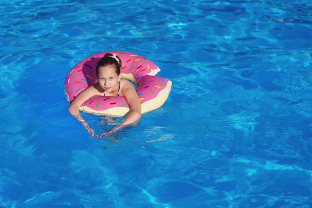 Mädchen Teenager in einem Badeanzug schwimmt mit einem aufblasbaren Ring im Pool mit blauem Wasser.