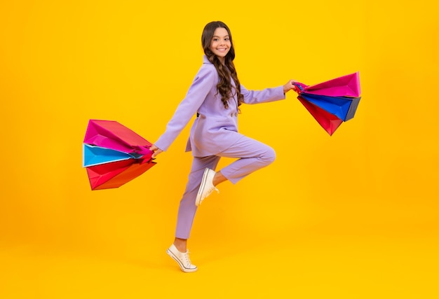 Mädchen Teenager mit Einkaufstüten isoliert auf gelbem Hintergrund Laufen und springen Einkaufs- und Verkaufskonzept
