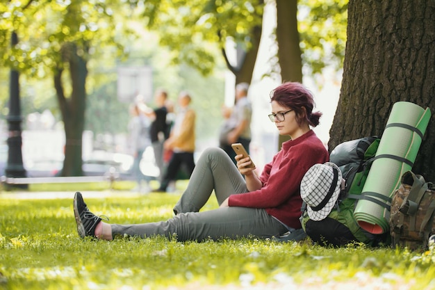 Mädchen teenager tourist mit rucksack blick auf smartphone im stadtpark, teleaufnahme