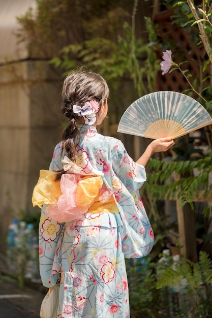 Mädchen trägt einen Kimono Yukata und hält einen Ventilator im Garten in Kyoto, Japan.
