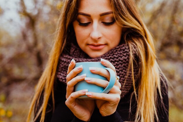 Mädchen trägt Strickpullover und Schal und genießt im Herbst ein heißes Getränk im Freien Herbststimmung und Lebensstil